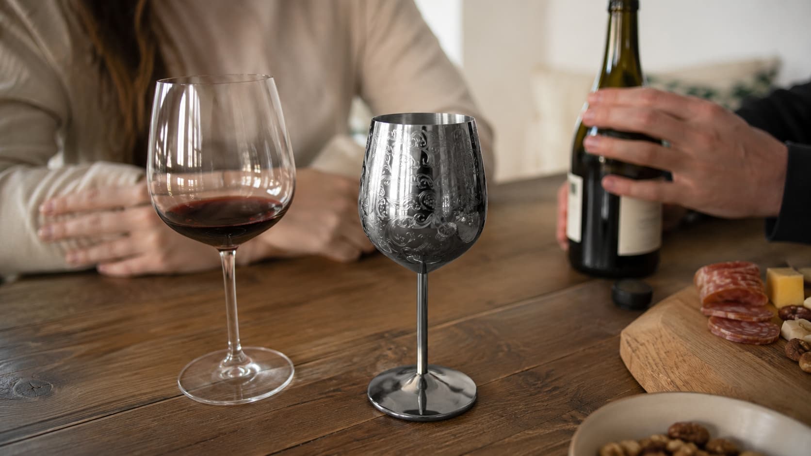 Etched stainless steel wine glass beside a traditional glass wine glass with red wine at a dinner table