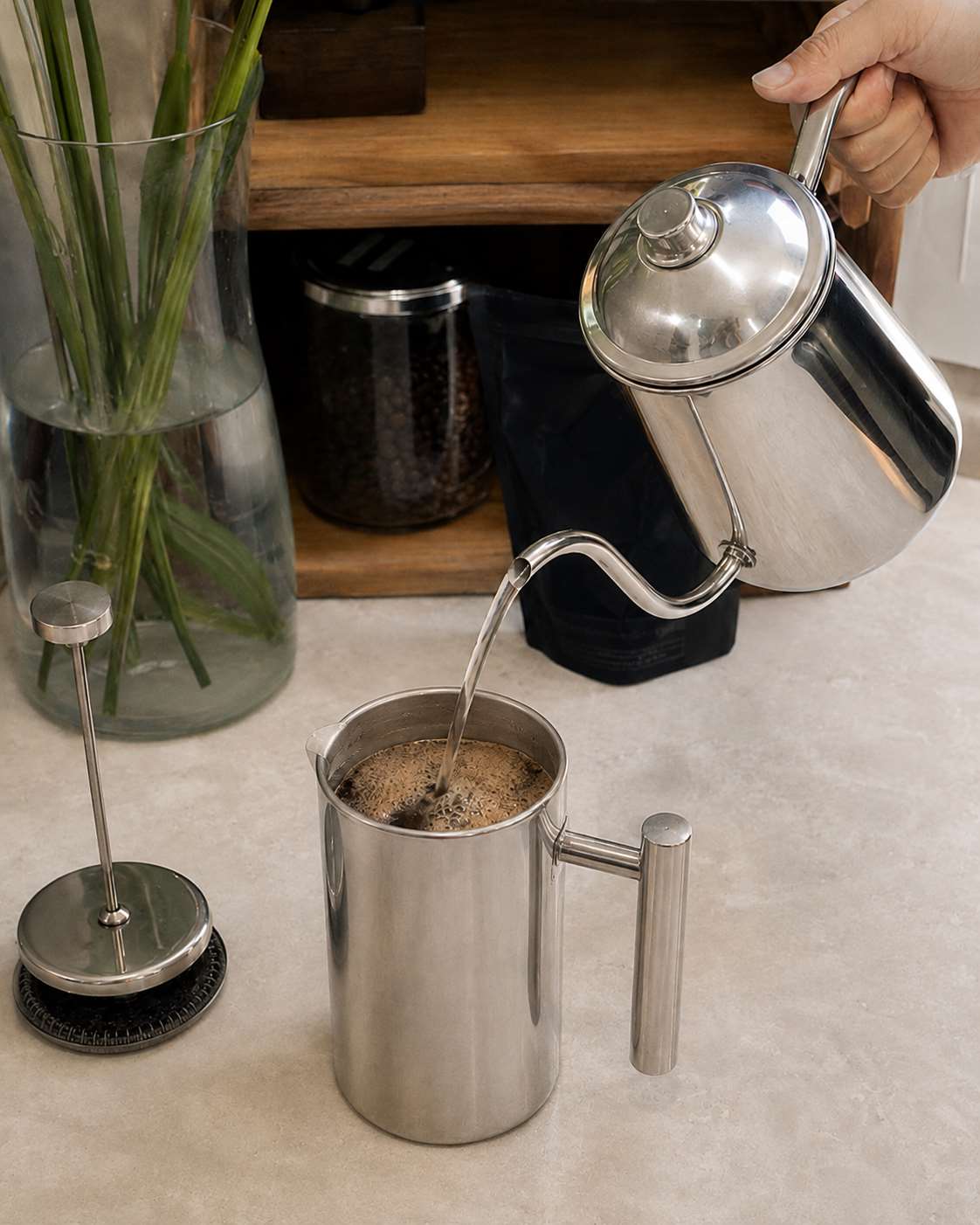 Hot water being poured into a stainless steel French press during the brewing process.